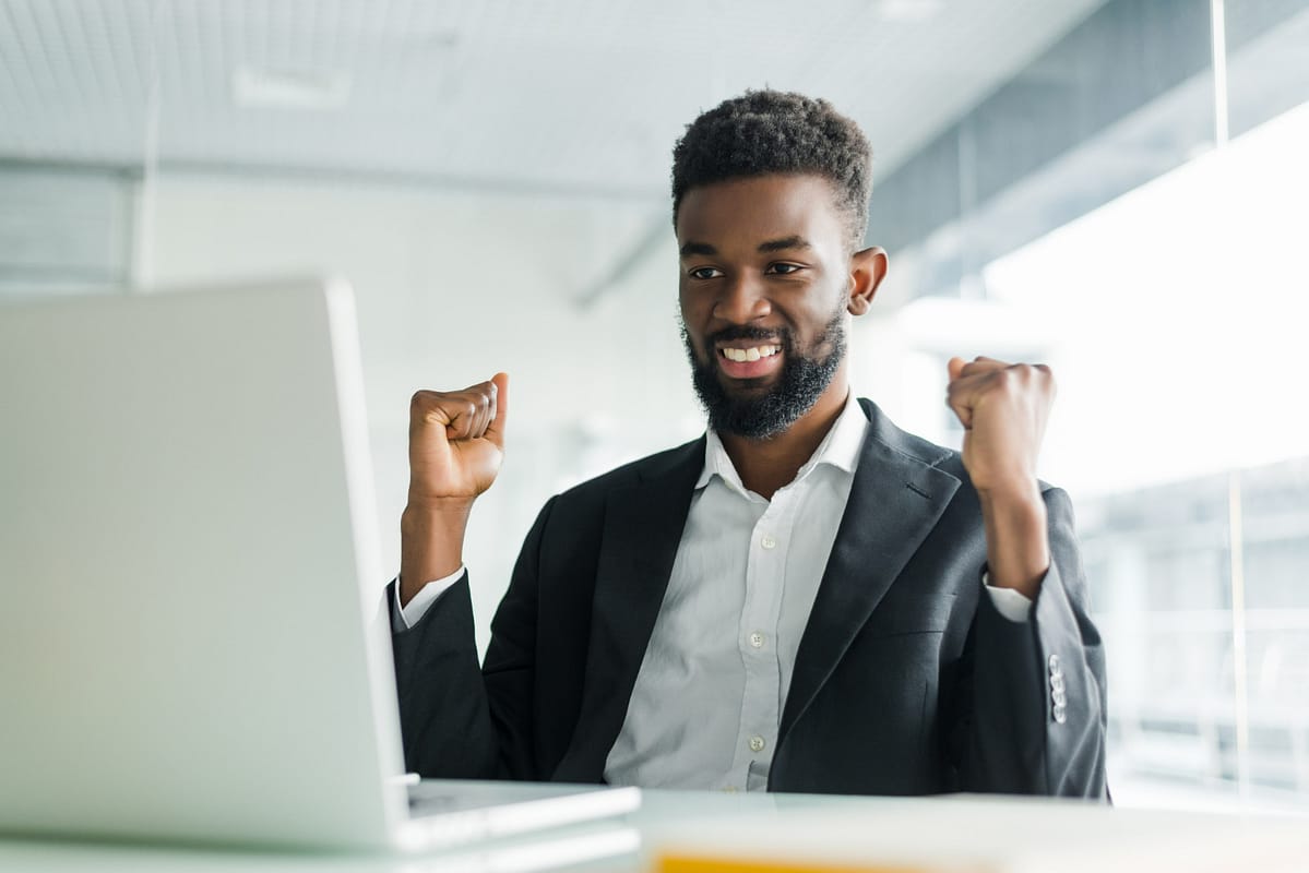 happy-african-american-businessman-suit-looking-laptop-excited-by-good-news-online-black-man-winner-sitting-office-desk-achieved-goal-raising-hands-celebrating-business-success-win-result